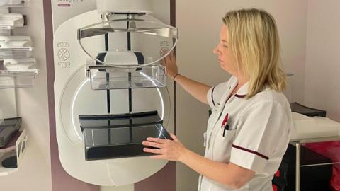 A nurse in a white coat holding a white screening machine