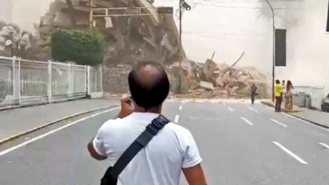 A man stands on a street staring towards a collapsed building.