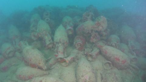 Dozens of barnacle-crusted jars seen on the sea bed.