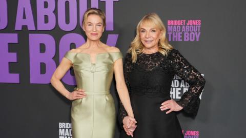 Renee Zellweger and Helen Fielding, both in dresses, hold hands on the red carpet for Bridget Jones: Mad About the Boy