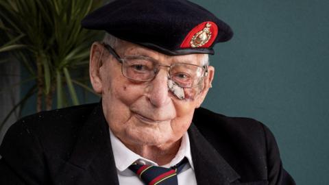 James "Jim" Wren. He is an elderly man with white short hair. He is wearing a Royal Navy hat, reading glasses, a white shirt, black blazer and a red, black and gold striped tie. He is smiling.