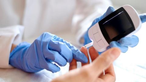 A doctor uses a glucometer to take a blood glucose reading from a patient.