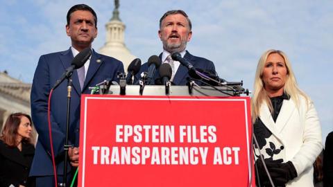 Representatives Ro Khanna, Thomas Massie and Marjorie Taylor Greene speak behind a red sign that reads "Epstein Files Transparency Act"