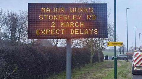 An illuminated sign at the side of the road warning of delays due to roadworks at Stokesley Road.