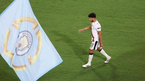 Matheus Nunes looks dejected as he walks off the pitch, with a Manchester City flag in the foreground