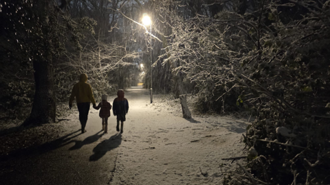  An adult and two young children walking on a snowy street at night-time