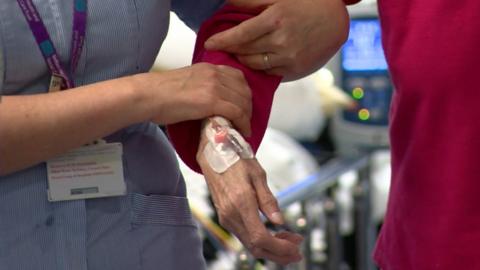 A nurse holds the arm of an elderly patient