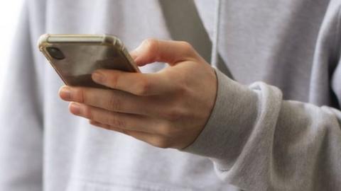 Teenage boy in grey hoodie holds phone