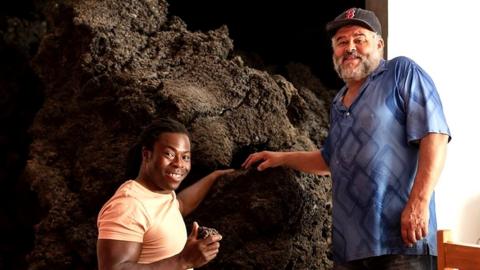 Romero with Ade inside his front room surrounded by volcanic rock