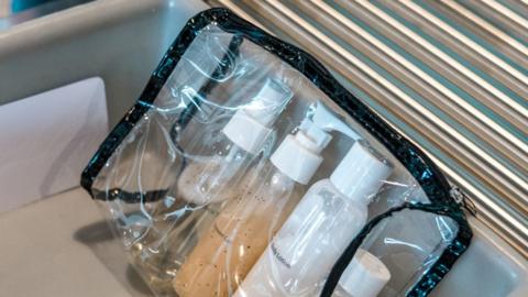 Four small bottles of liquid in a clear plastic zip-up case. It is on a plastic tray on an airport security conveyor belt