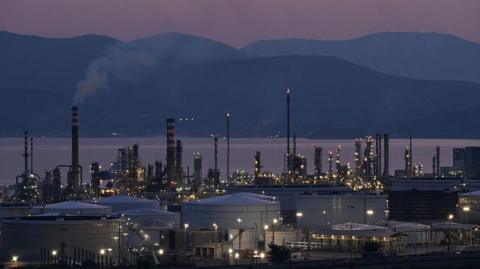 A view of the Motor Oil refinery in Agioi Theodoroi near Corinth, Greece during the evening. Behind the refinery, the sea and hills are visible but dark.