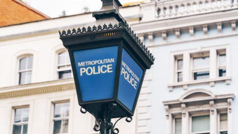 A blue Metropolitan Police lamp post with the words Metropolitan Police in white writing. There's a white building in the background 