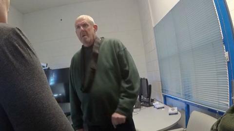 Old man with short white hair in a green jumper.