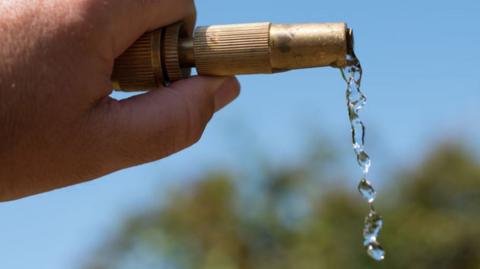 Water dripping from the end of a hosepipe being held up, with a blue sky behind