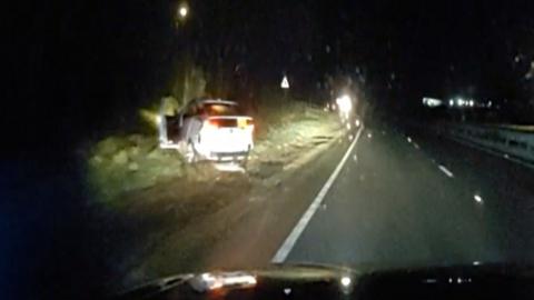 Grainy images of a white car illuminated by teh headlights of another car on a dark road