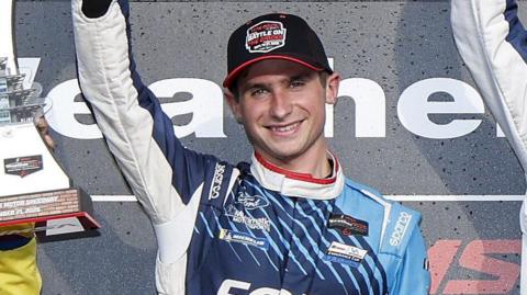 Seb Priaulx raises his arm in celebration while on the podium