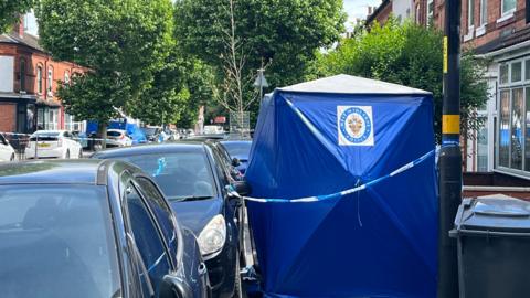 West Midlands Police blue forensic tent on a cordoned residential street with parked cars and terraced houses