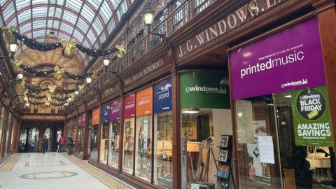 The multi-coloured shop front of J.G Windows. Musical instruments can be seen through the windows. Christmas decorations are hung in the arcade hallway outside.