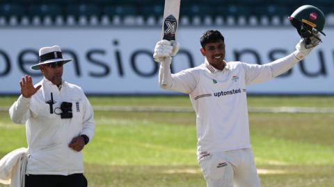 Rishi Patel raises his bat and helmet after completing a century against Kent