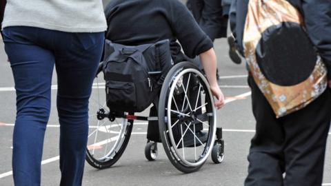 A teenage child in a wheelchair in a school playground. All faces are obscured so you can not identify any individuals in this illustrative picture to go with the story.