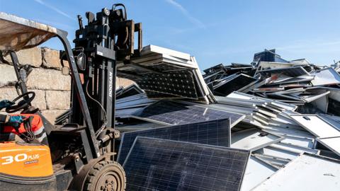 A fork-lift drops solar panels in a heap