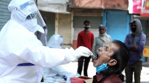 An Indian doctor takes samples from a worker during COVID-19 routine testing at a local market on May Day