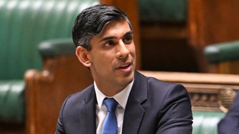 Sunak looking away from camera while wearing a suit and blue tie as he speaks in Parliament on 23 January