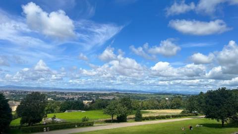 Broken white clouds in a blue sky above parkland