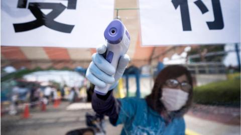 An employee wearing a face mask measures a visitor's temperature at a theme park in Japan.