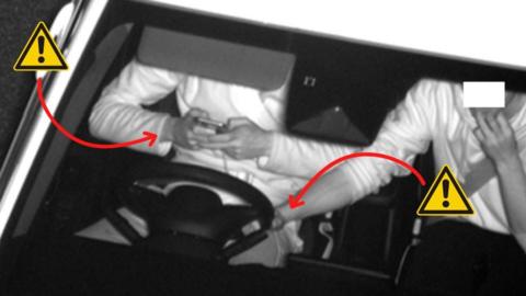 Motorist using a mobile phone while passenger holds steering wheel