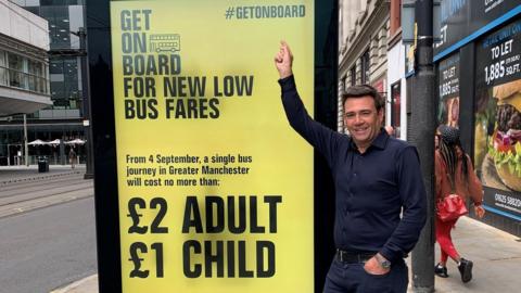 Andy Burnham pointing to a cheaper bus fare advertisement