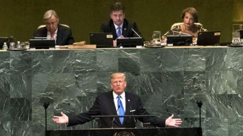 Donald Trump addresses the United Nations with outstretched arms in front of a podium emblazoned with the UN emblem