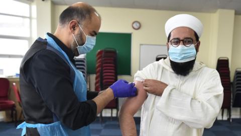 Man administering another man with the Covid vaccine in the hall of a mosque