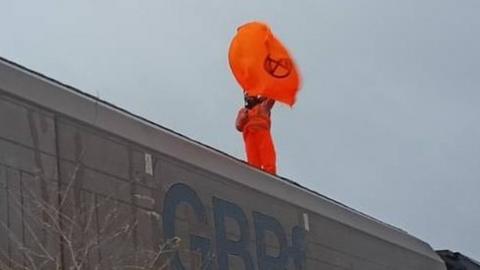 Activist wearing orange suite waving an orange flag on top of a train