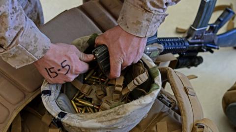 A US Marine unloads ammunition from a rifle magazine into his helmet after arriving in Kandahar