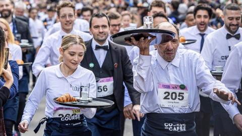 A young waitress and an older waiter carry trays during the race