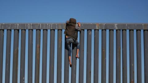 A migrant, part of a caravan of thousands from Central America trying to reach the United States, climbs the border fence