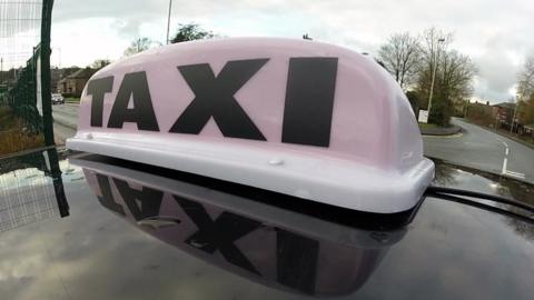 General view of a TAXI sign on the roof of a licensed mini cab.