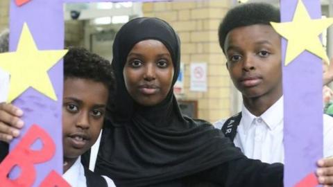A woman in a head scarf with two young boys either side looking at the camera