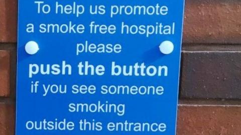 A sign that says 'push the button' if you see someone smoking outside