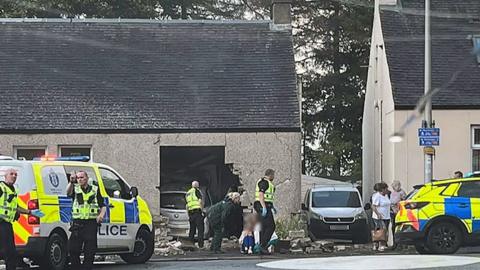 Police attending the scene around a car which crashed into a house