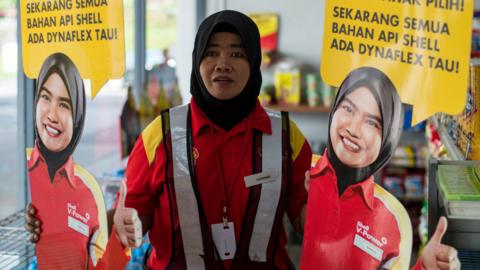 A Shell petrol station employee holds up life-sized cutouts depicting a female staff member, pictured in uniform with a black Muslim headscarf and placed beside individual self-serve petrol pumps as part of a promotional campaign, as they were pulled from display at a Shell station in Bentong, some 70 kms north of Kuala Lumpur in nearby Pahang state on July 4, 2017
