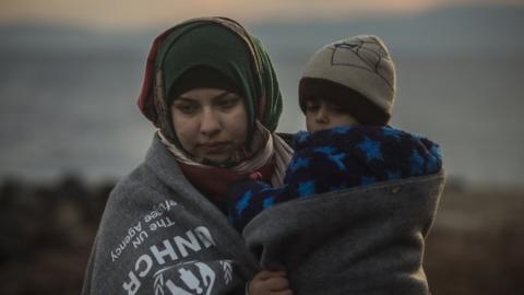 A migrant woman holds a child on a beach near the town of Mytilene