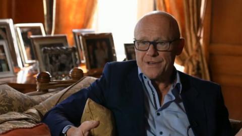John Caudwell sitting in a living room