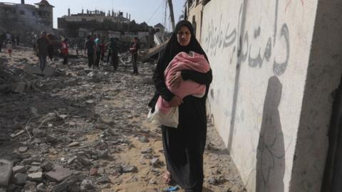 A woman carries a baby as Palestinians search for usable items among the debris of destroyed building following the Israeli attacks on the al-Salam Neighborhood in Rafah, Gaza on May 5, 2024