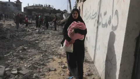 A woman carries a baby as Palestinians search for usable items among the debris of destroyed building following the Israeli attacks on the al-Salam Neighborhood in Rafah, Gaza on May 5, 2024