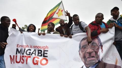 People wave a Zimbabwean national flag and carry banners during a demonstration demanding the resignation of Zimbabwe"s president on November 18, 2017 in Harare.