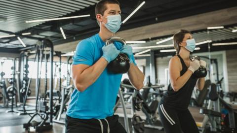 Man and woman wearing masks working out at a gym