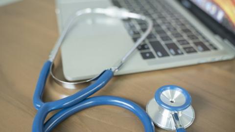 A stethoscope on a desk with a silver laptop in the background