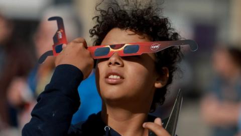 Junior Espejo looks through eclipse glasses being handed out by NASA on April 08, 2024, in Houlton, Maine.